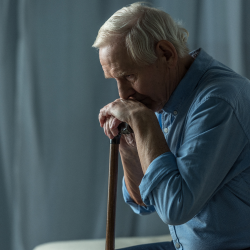 Despondent elderly man with a cane resting his head on his hands